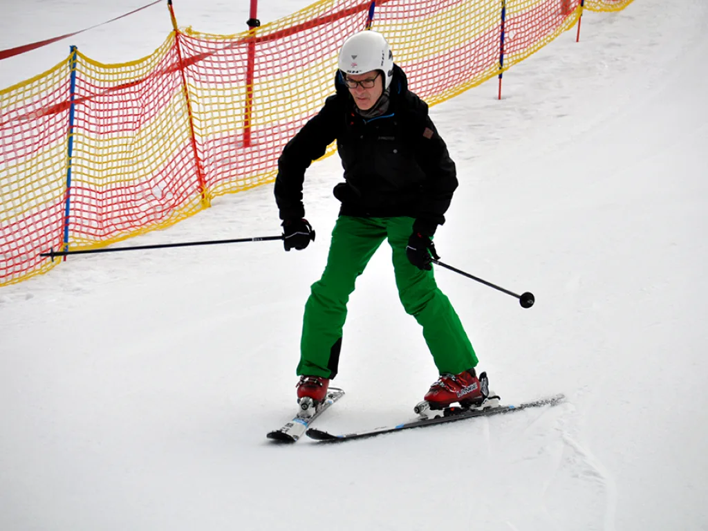 Skifahrer in grüner Hose vor dem bunten Absperrnetz.